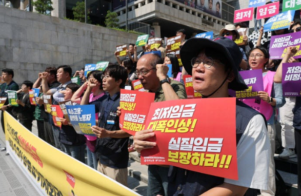 15일 서울 종로구 세종문화회관 계단에서 열린 ‘2027년 적용 최저임금 노동계 요구안 발표 기자회견’ 참석자들이 내년 최저임금 ‘1만2000원’을 요구하며 퍼포먼스를 선보이고 있다. 연합뉴스
