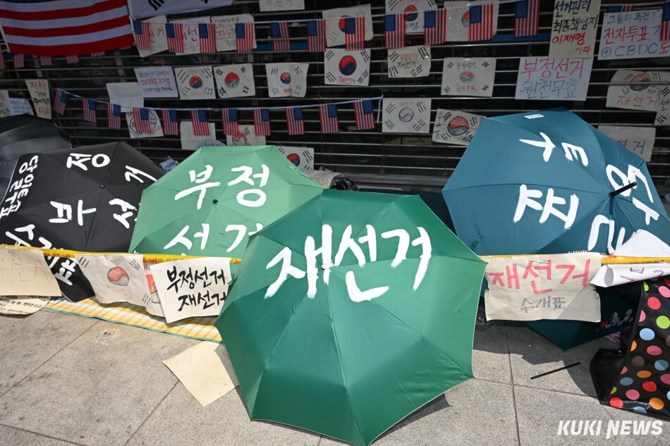 잠실 개표소 시위가 2주째 이어지는 지난 18일 서울 송파구 올림픽공원 핸드볼경기장 출입구에 놓인 우산에 투표용지 부족 사태를 규탄하는 문구가 적혀 있다. 임은재 기자